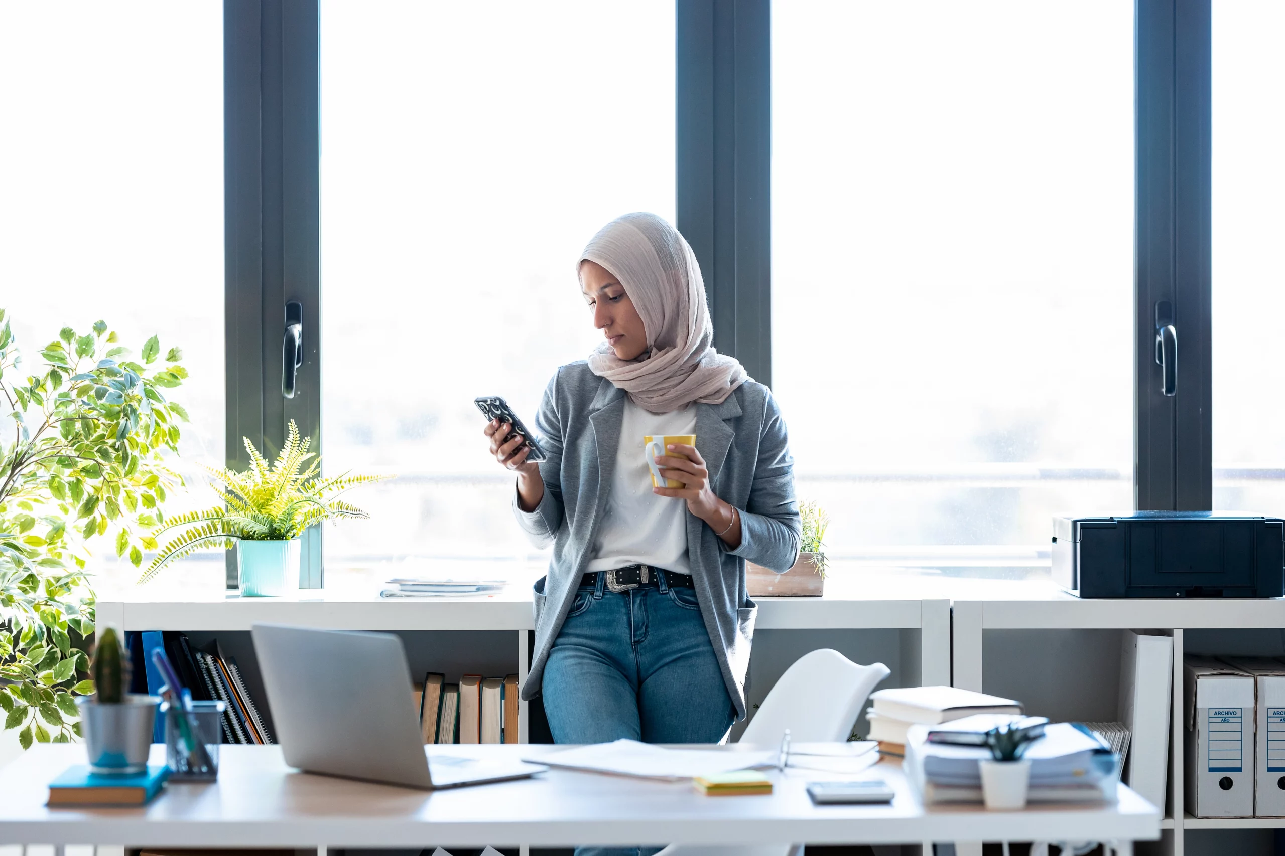 Business Frau im Büro, welche ihren Kaffee trinkt und auf das Handy schaut