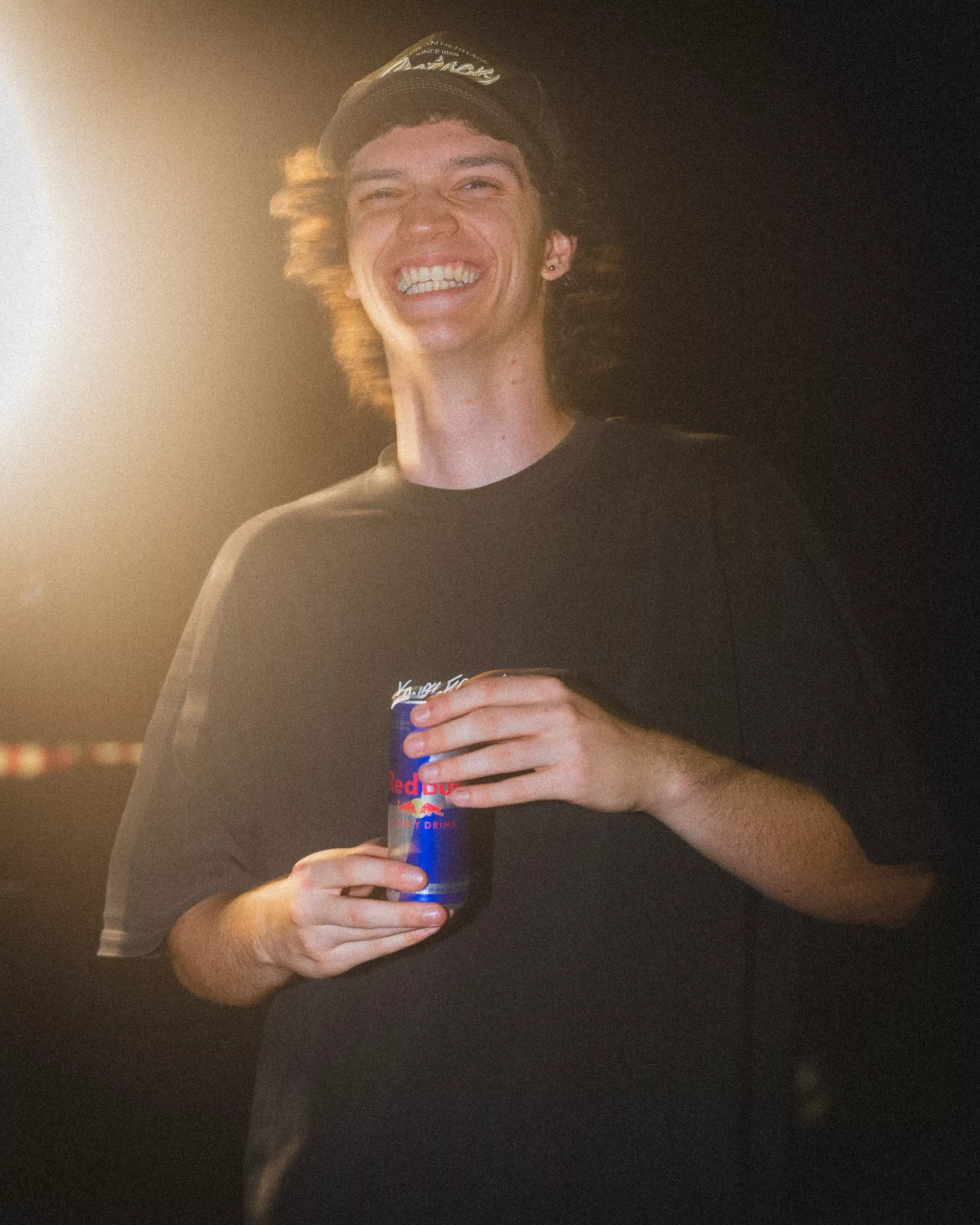 Ein lachender junger Mann mit einer Red Bull-Dose in der Hand, eingefangen in dynamischer Beleuchtung – ein authentischer Moment am Set der Video Agentur twoseconds
